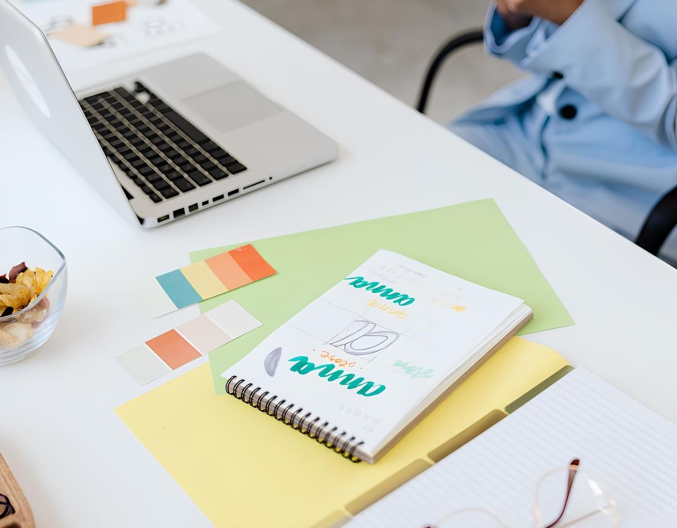 Frau arbeitet an einem Laptop am Schreibtisch, umgeben von einem Notizbuch und Stiften.