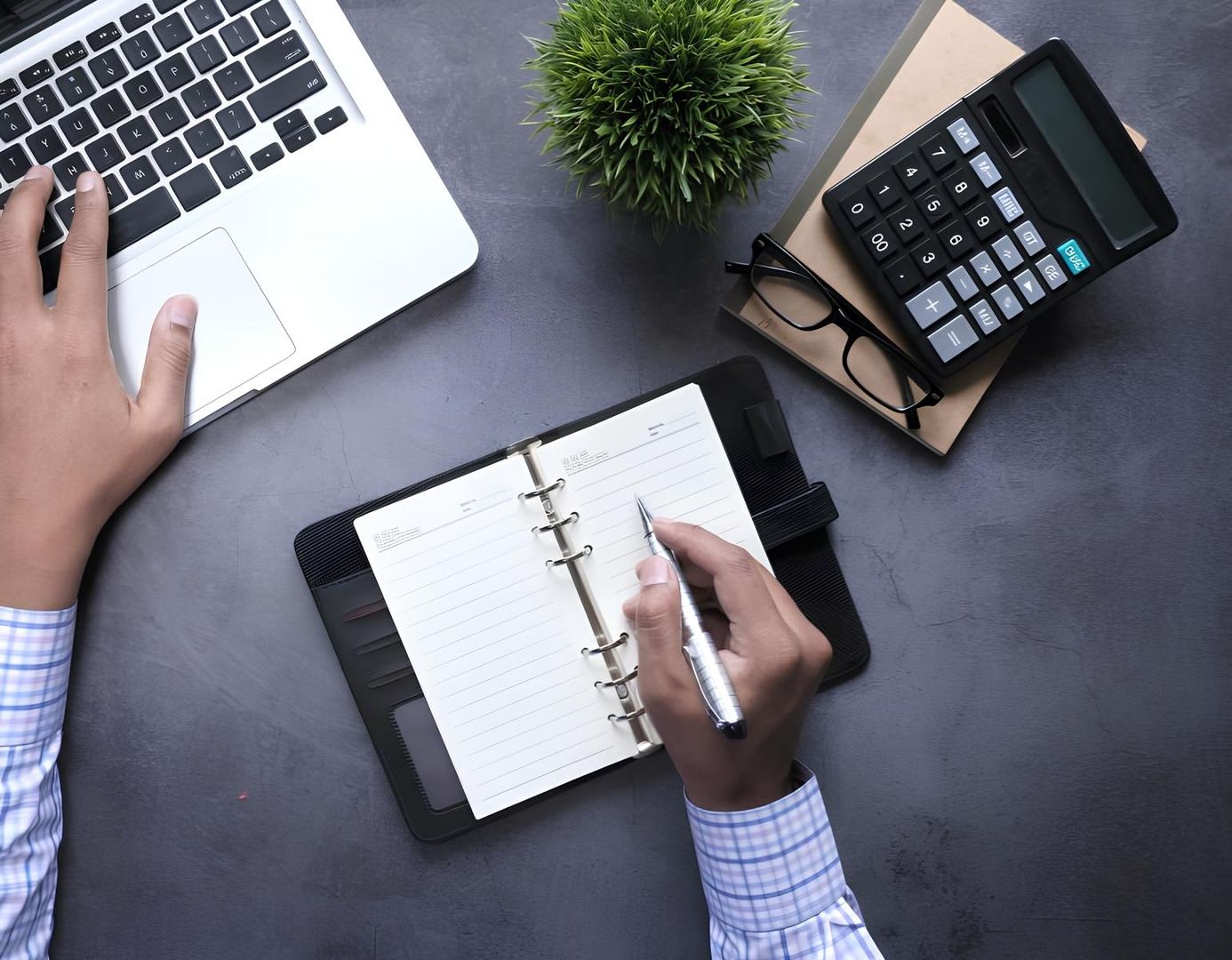 Die Hände eines Geschäftsmannes schreiben in ein Notizbuch, während ein Laptop auf dem Schreibtisch steht.